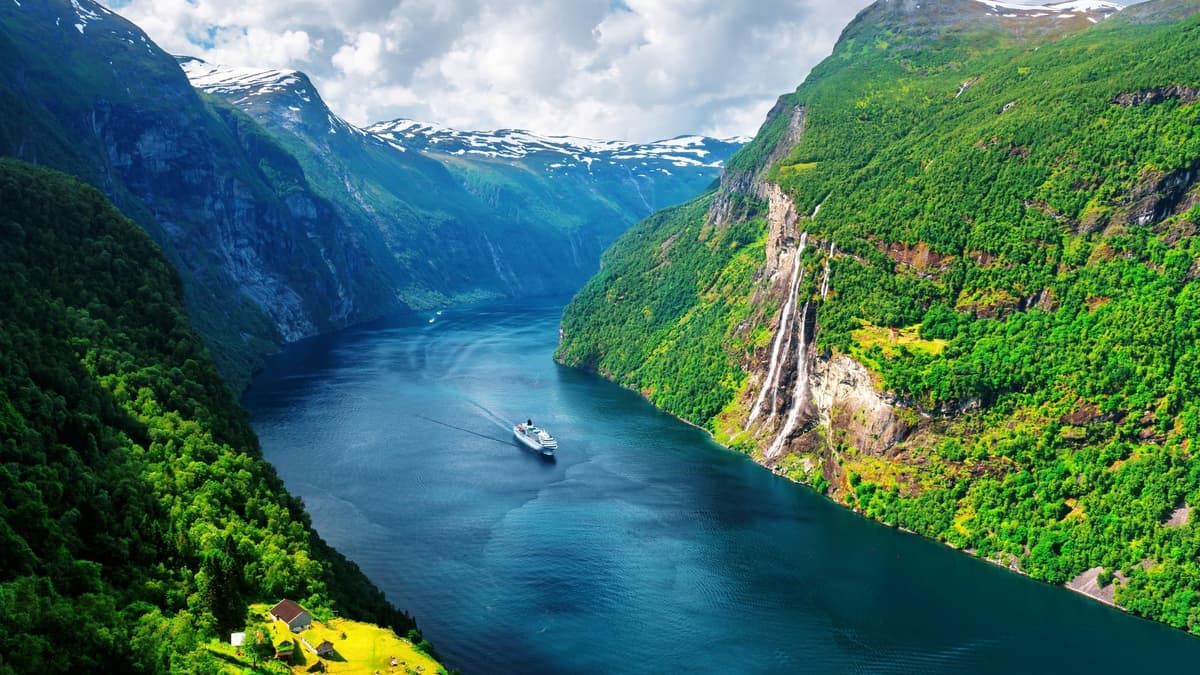 Evening view of a Norwegian fjord with steep green mountains, cascading waterfalls, and a cruise ship sailing through calm waters, symbolizing Norway’s advanced digital invoicing ecosystem supported by DDD Invoices’ API solution.