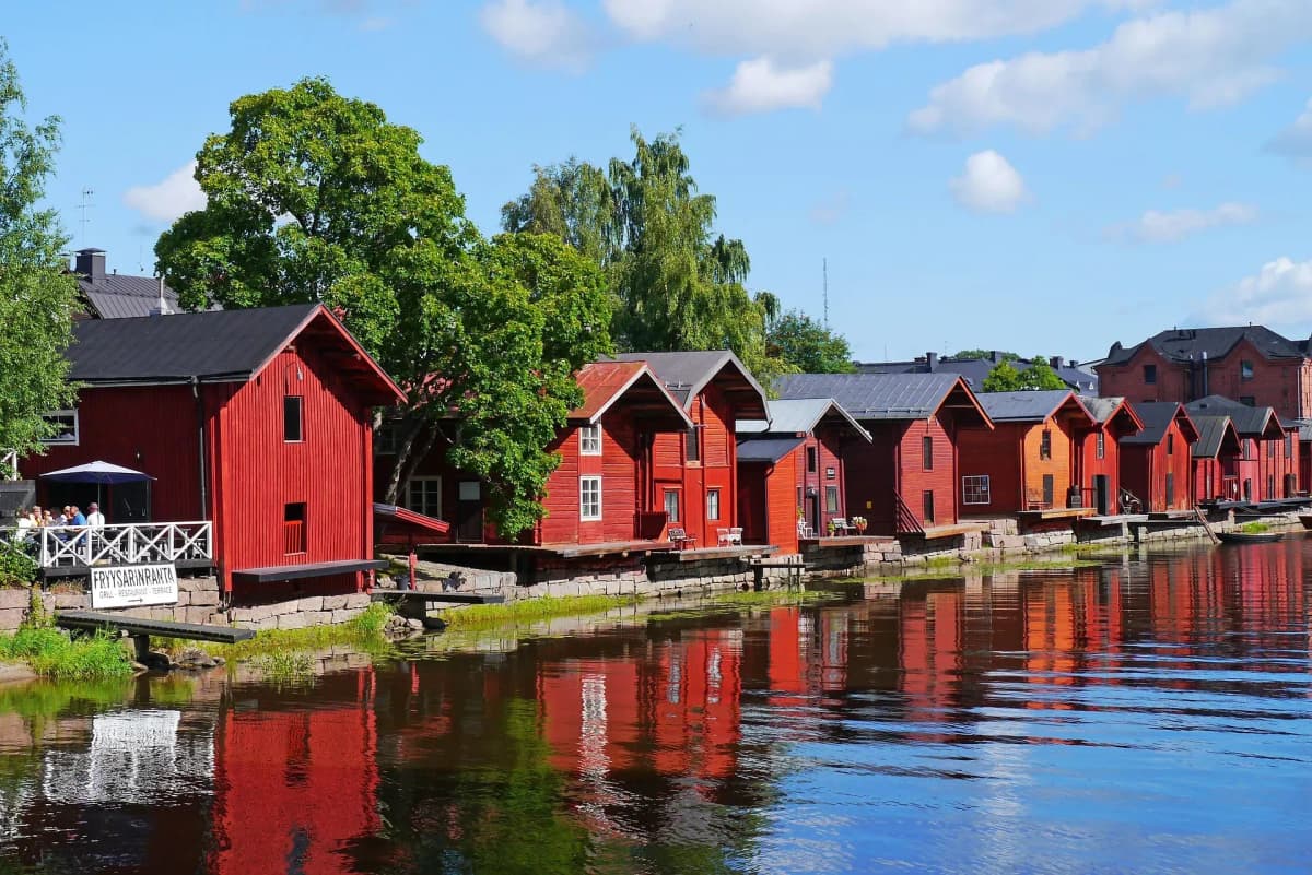 DDD Invoices supporting e-invoicing in Finland, featuring traditional red wooden riverside houses reflected in calm water under a clear blue sky.