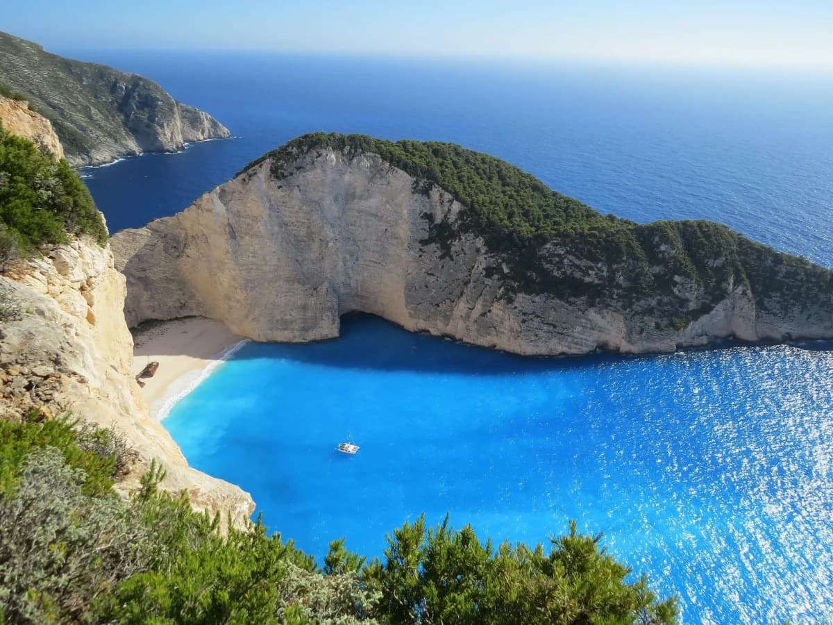DDD Invoices supporting e-invoicing in Greece, featuring a coastal bay with turquoise water, steep cliffs, and a sandy beach with a boat.