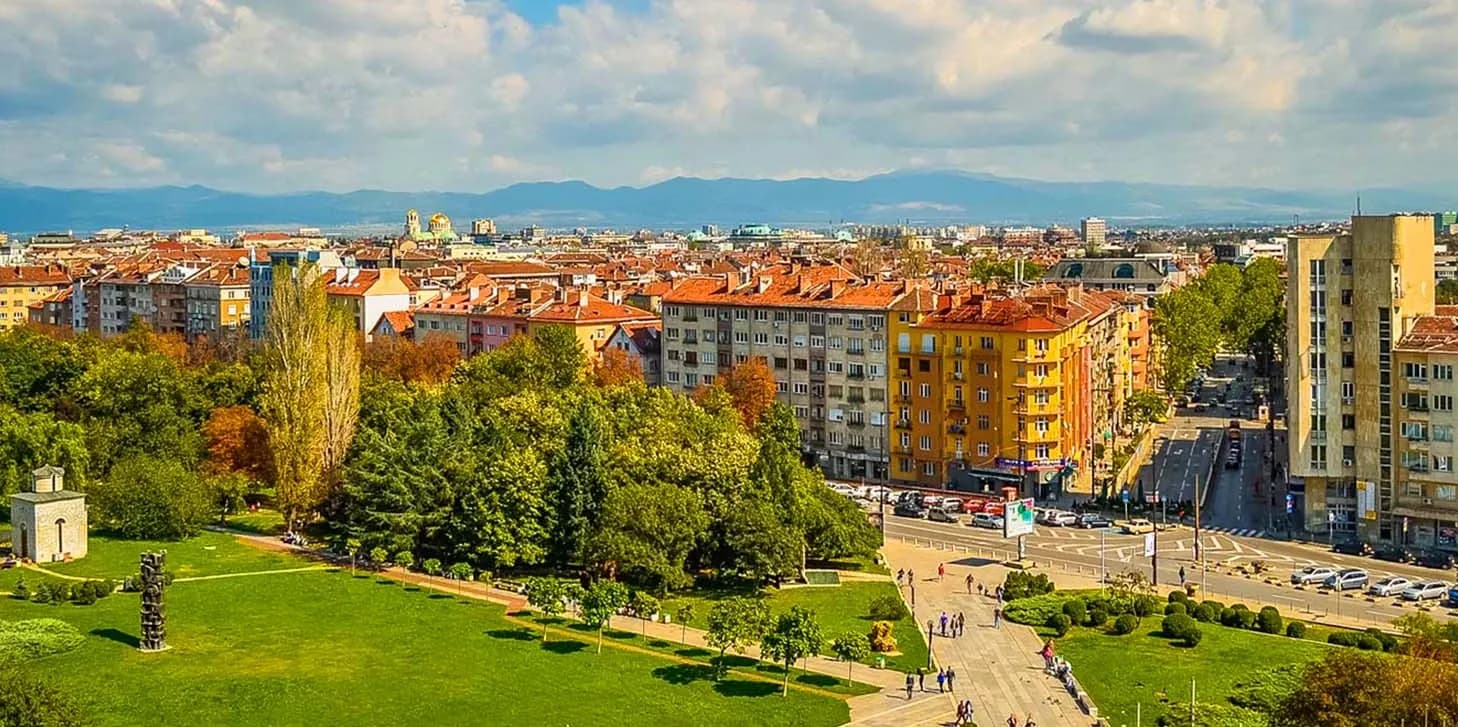 Vibrant cityscape of Sofia, Bulgaria, with colorful buildings, parks, and mountain views, showcasing the modernization of business processes supported by DDD Invoices’ e-invoicing solutions in Bulgaria.