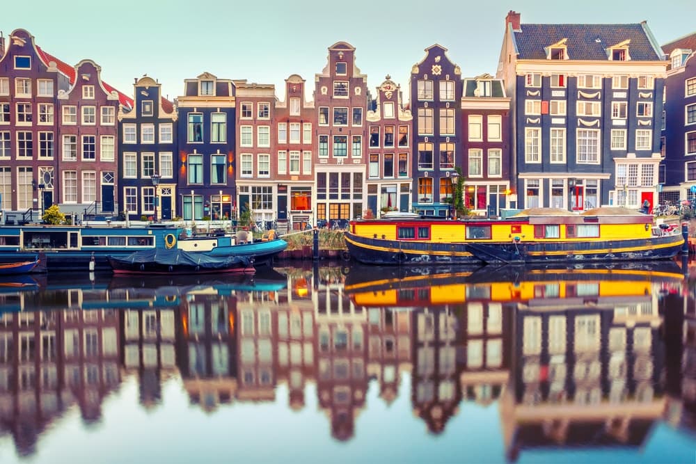 Canal-side view of Amsterdam with colorful historic townhouses and houseboats reflected in calm water, highlighting the Netherlands’ connected digital economy supported by DDD Invoices’ API-driven e-invoicing solutions.