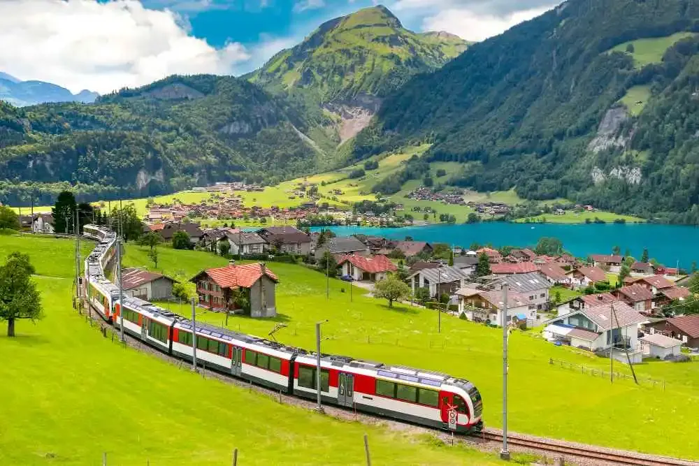A scenic Swiss train passing through a picturesque mountain valley with charming villages and a turquoise lake, as Switzerland continues its move toward nationwide e-invoicing adoption with support from DDD Invoices API solutions.