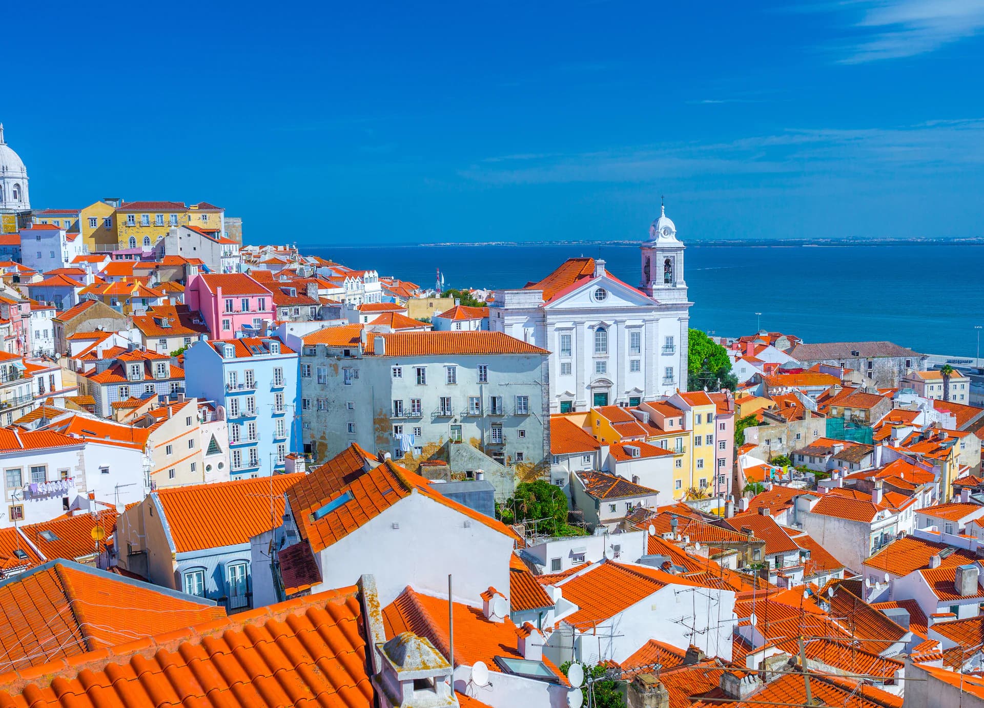 Charming coastal view of Lisbon, Portugal, where colorful historic buildings and iconic red rooftops overlook the Atlantic, all made more efficient with DDD Invoices powering modern digital invoicing solutions.